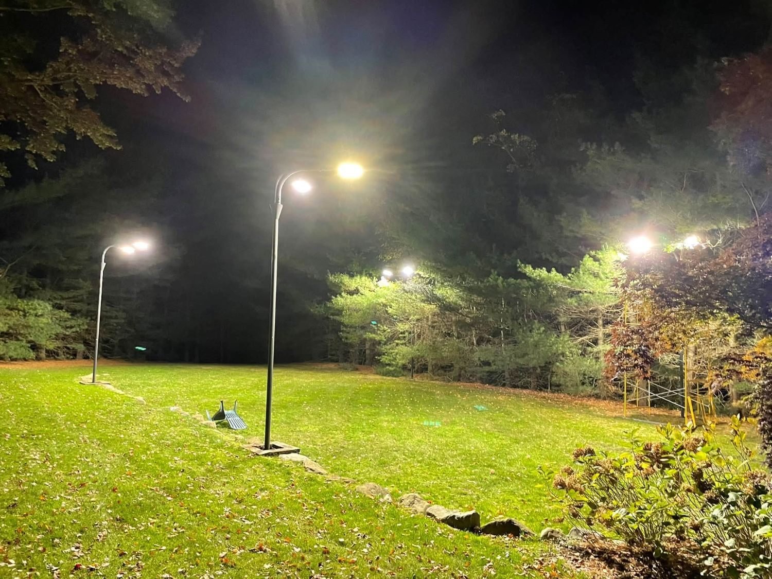 Postes de luz exteriores iluminando un jardín grande de noche
